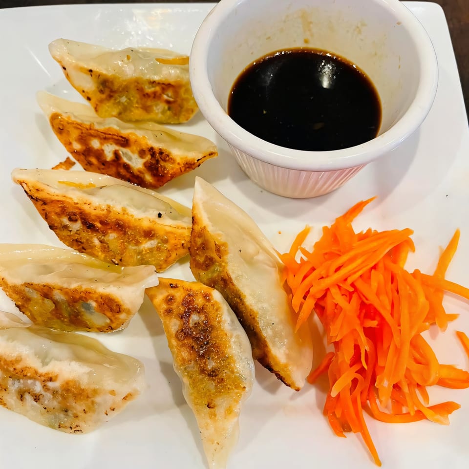 Pan-fried dumplings with a side of shredded carrots and a dipping sauce at Pho Boca.