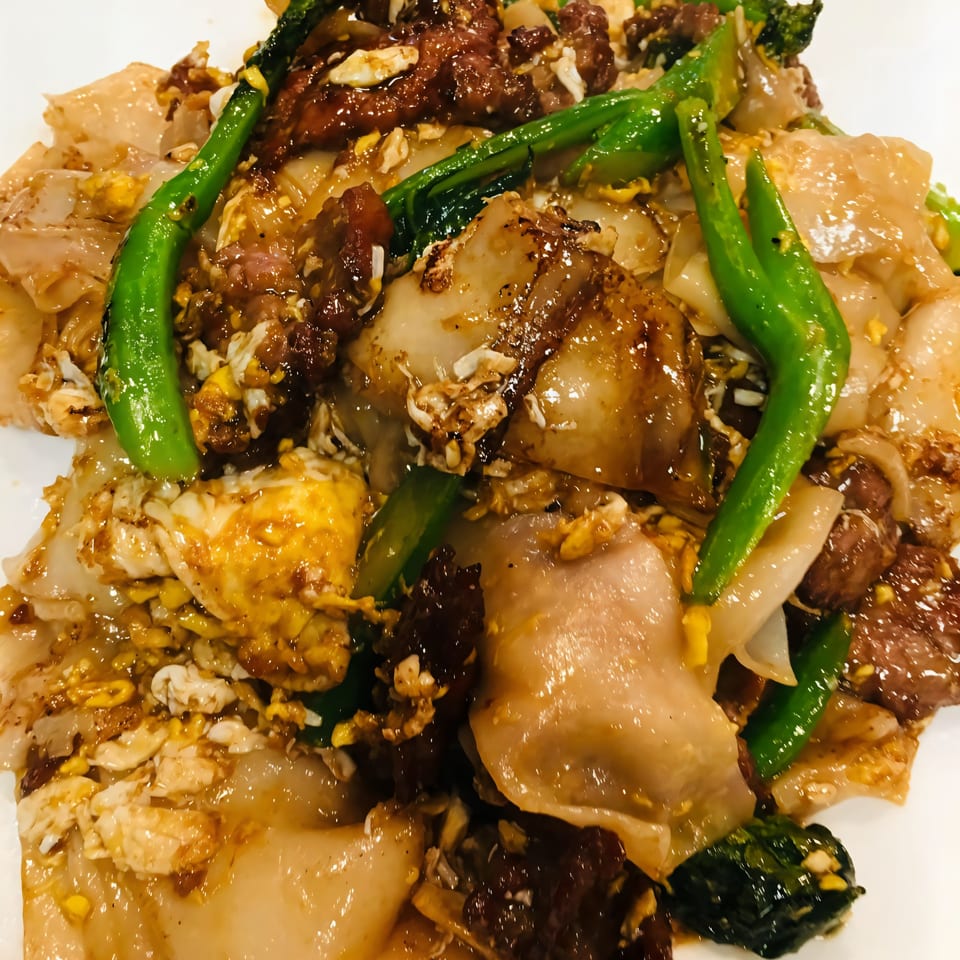 Close-up of Vietnamese stir-fried noodles with beef, eggs, and green vegetables on a white plate.