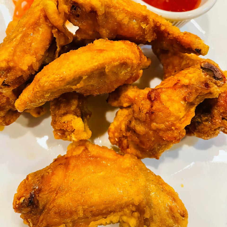 Crispy golden-brown fried chicken wings, some with visible bones, served on a white plate with a red dipping sauce.